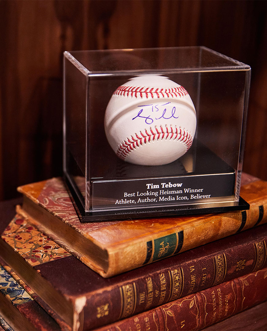 Baseball in a glass display that is signed by Tim Tebow; a famous athlete 