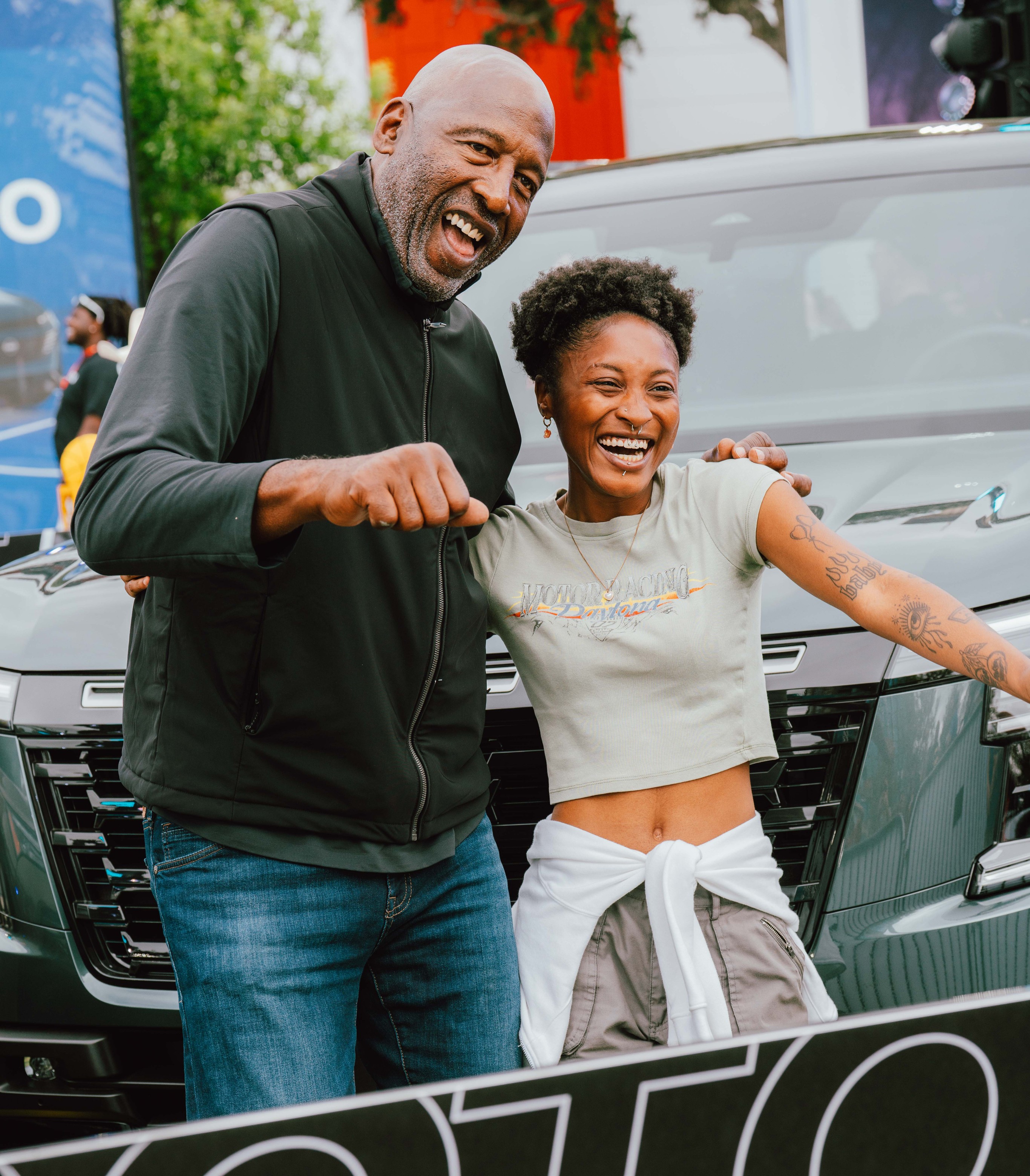 Two fans posing in front of a Nissan and smiling.